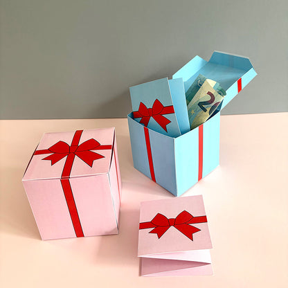 Offene Gutscheinbox mit Schleifen-Design in Rosa und Blau – befüllt mit Geldschein und Klappkarte